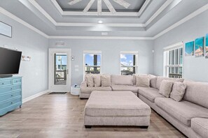 A spacious living room with a large sectional sofa, a television, and a blue dresser. - Hot Tub | Sleeps 14 | Beach View (Crystal Beach)
