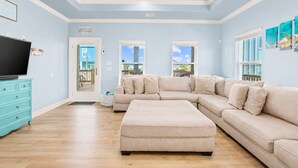 Un salon avec un canapé d’angle, un téléviseur et une commode de couleur turquoise.