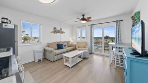 A modern living room with a sofa, armchairs, a coffee table, a TV, and a balcony with a view. - Plantation 3201 with Outdoor/Indoor pools (Gulf Shores)