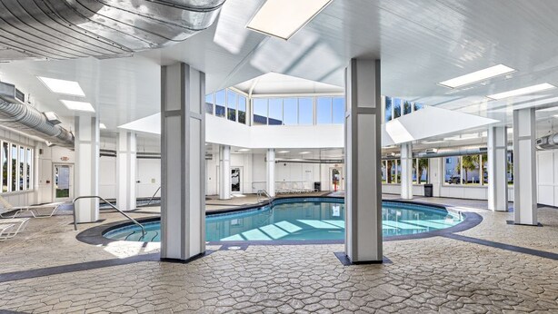 A modern indoor swimming pool with a geometric tile floor, large windows, and a high ceiling with skylights. - Plantation 3201 with Outdoor/Indoor pools (Gulf Shores)