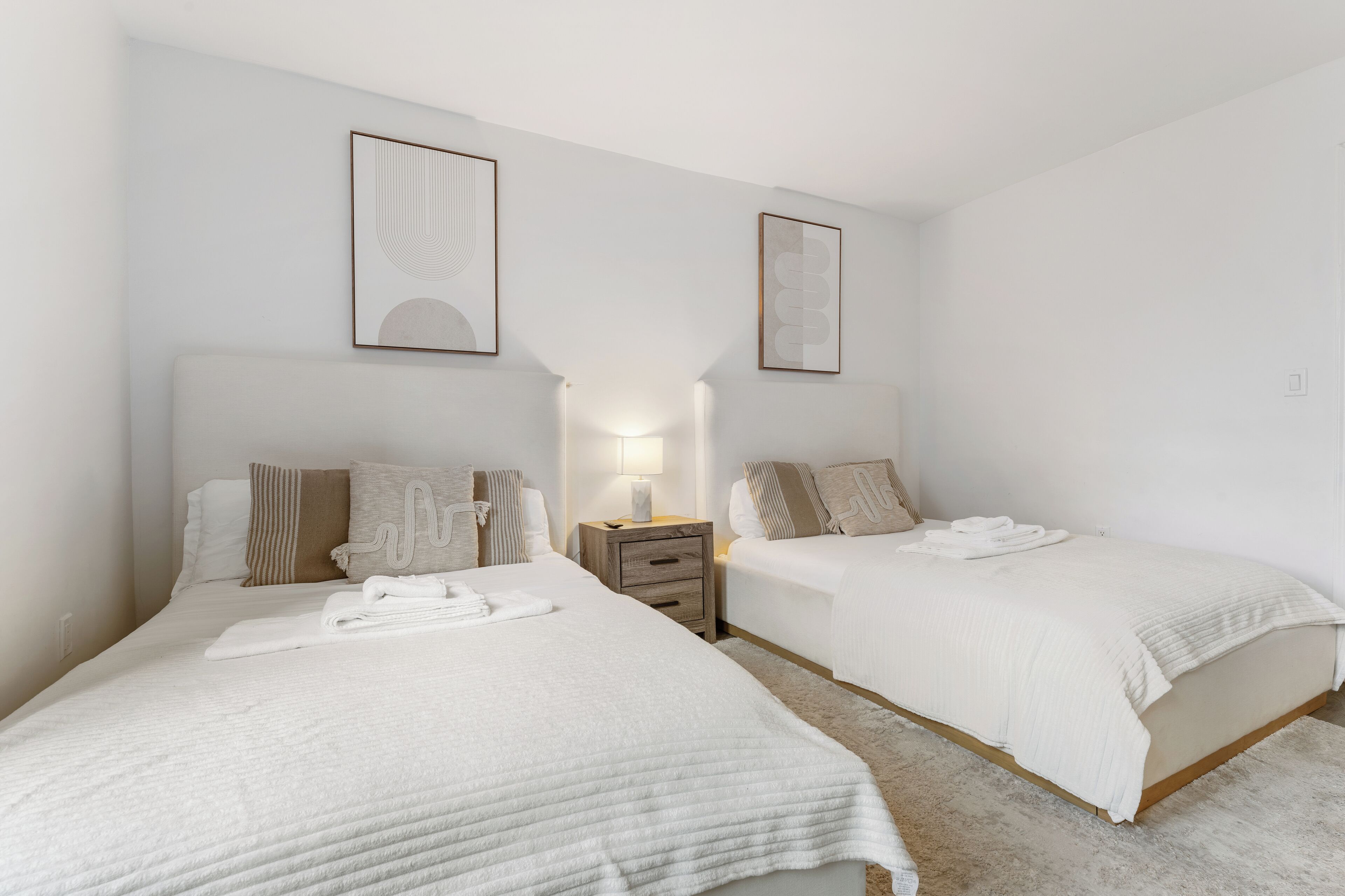 A hotel room with two beds, a nightstand, a lamp, and framed artwork on the walls.