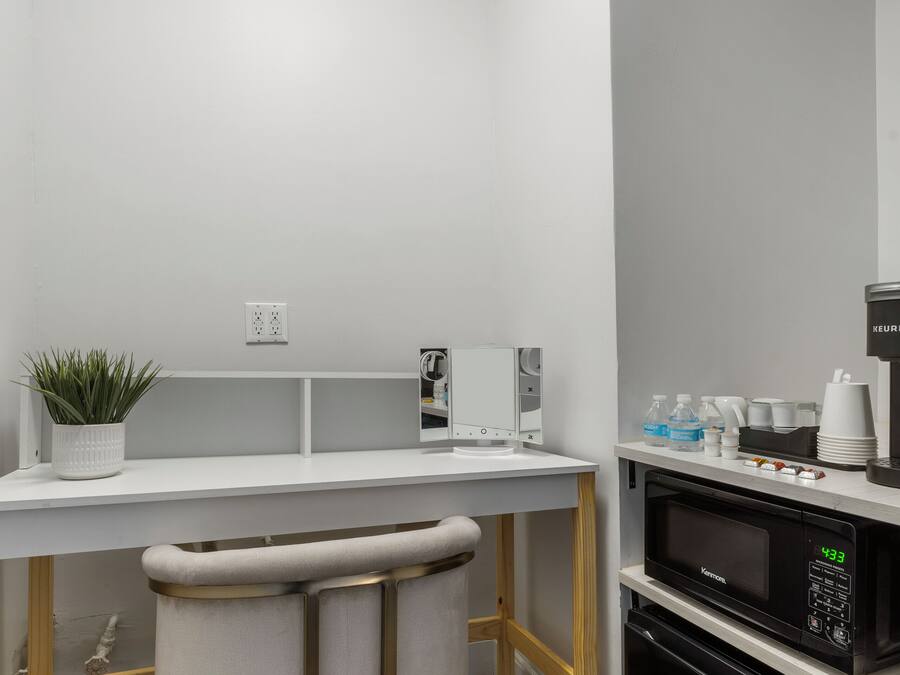A modern kitchen with a white countertop, a bar stool, a microwave, and a coffee machine.