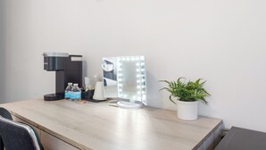 A hotel room with a wooden desk, a coffee machine, a mirror with lights, a potted plant, and a chair. - Bay Ridge ApartHotel (Brooklyn)