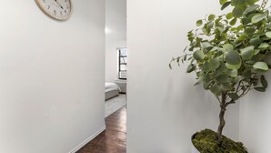 A hallway with a wooden floor, a wall-mounted clock, and a potted plant. - Bay Ridge ApartHotel (Brooklyn)