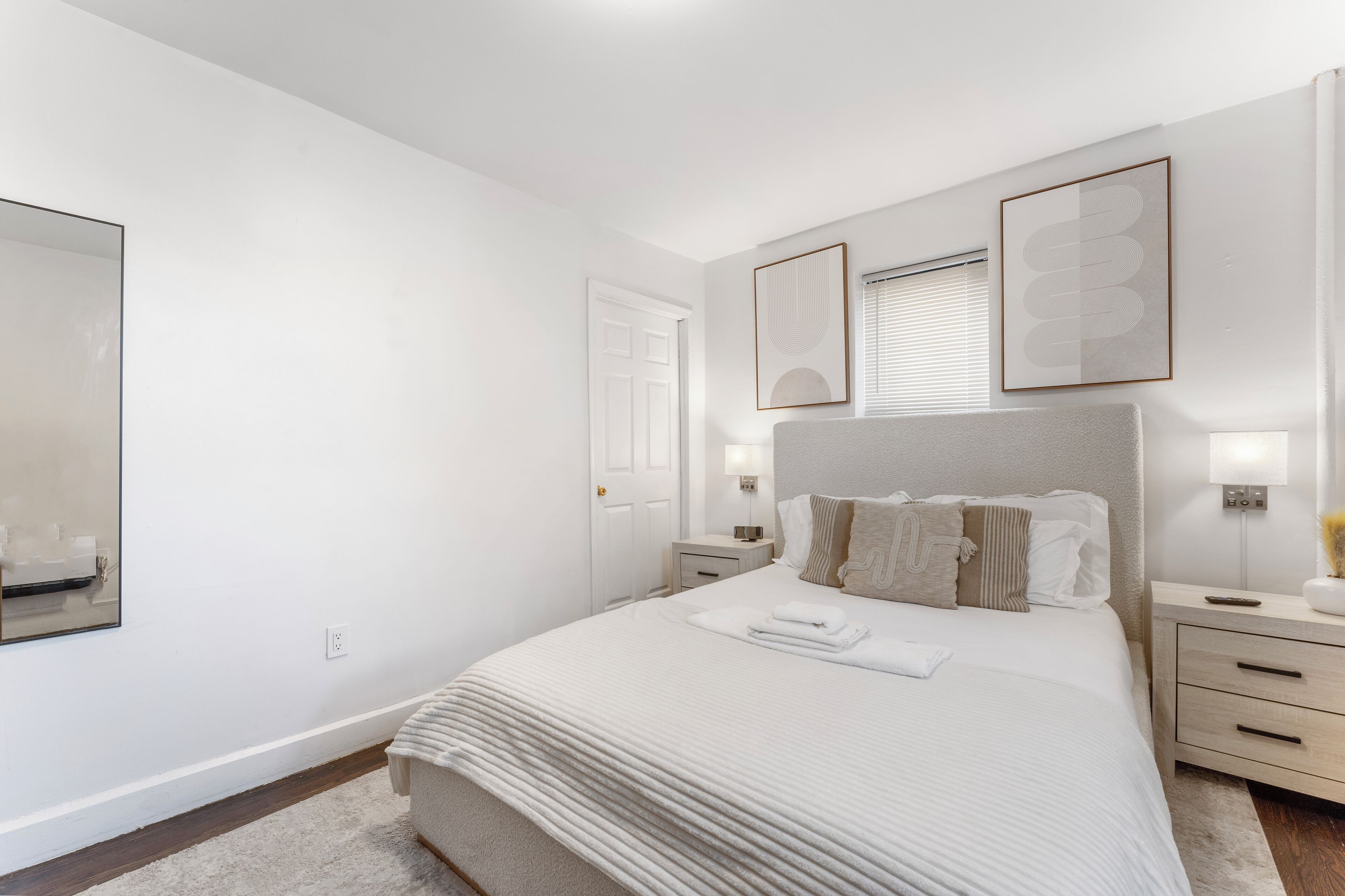 A modern bedroom with a large bed, bedside tables, a mirror, and framed artwork on the wall.