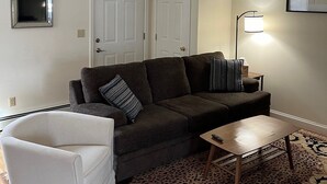 Un salon comprenant un canapé, un fauteuil, une table basse, une lampe et un tapis à motifs.