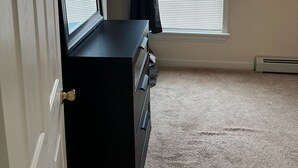 Une pièce avec une porte, une commode, une fenêtre avec des stores et un radiateur.