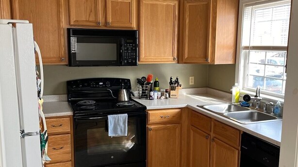 Une cuisine compacte avec des meubles en bois, une cuisinière noire, un four à micro-ondes et un lave-vaisselle.