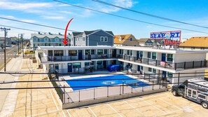 Hotel de diversos pisos amb zona de piscina, un senyal amb la paraula 'SEAPORT' i una furgoneta de servei de 'MORTON ELECTRIC'.