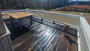 A wooden deck with a table and white railings, overlooking a forested area. - Cozy 3-bedroom 2 bath,5beds mobile home. Close to a boat launch. Covered parking (Many)