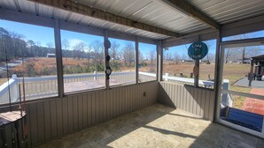 A covered porch with a view of a rural landscape, a wooden railing, and a sign reading "The Lake House." - Cozy 3-bedroom 2 bath,5beds mobile home. Close to a boat launch. Covered parking (Many)