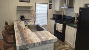 A kitchen with a wooden island, stainless steel appliances, and white cabinetry. - Cozy 3-bedroom 2 bath,5beds mobile home. Close to a boat launch. Covered parking (Many)