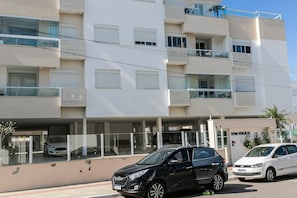 Un edificio de varios pisos con balcones, un coche estacionado en la entrada y un cartel con el número de la dirección.