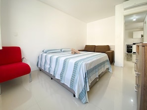 Un dormitorio con una cama, una silla roja, un sofá marrón y un armario de madera.