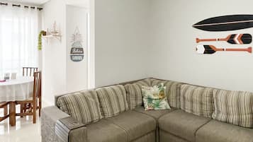 A living room with a sectional sofa, a dining table with chairs, and a wall with decorative items including a sailboat and paddleboards.