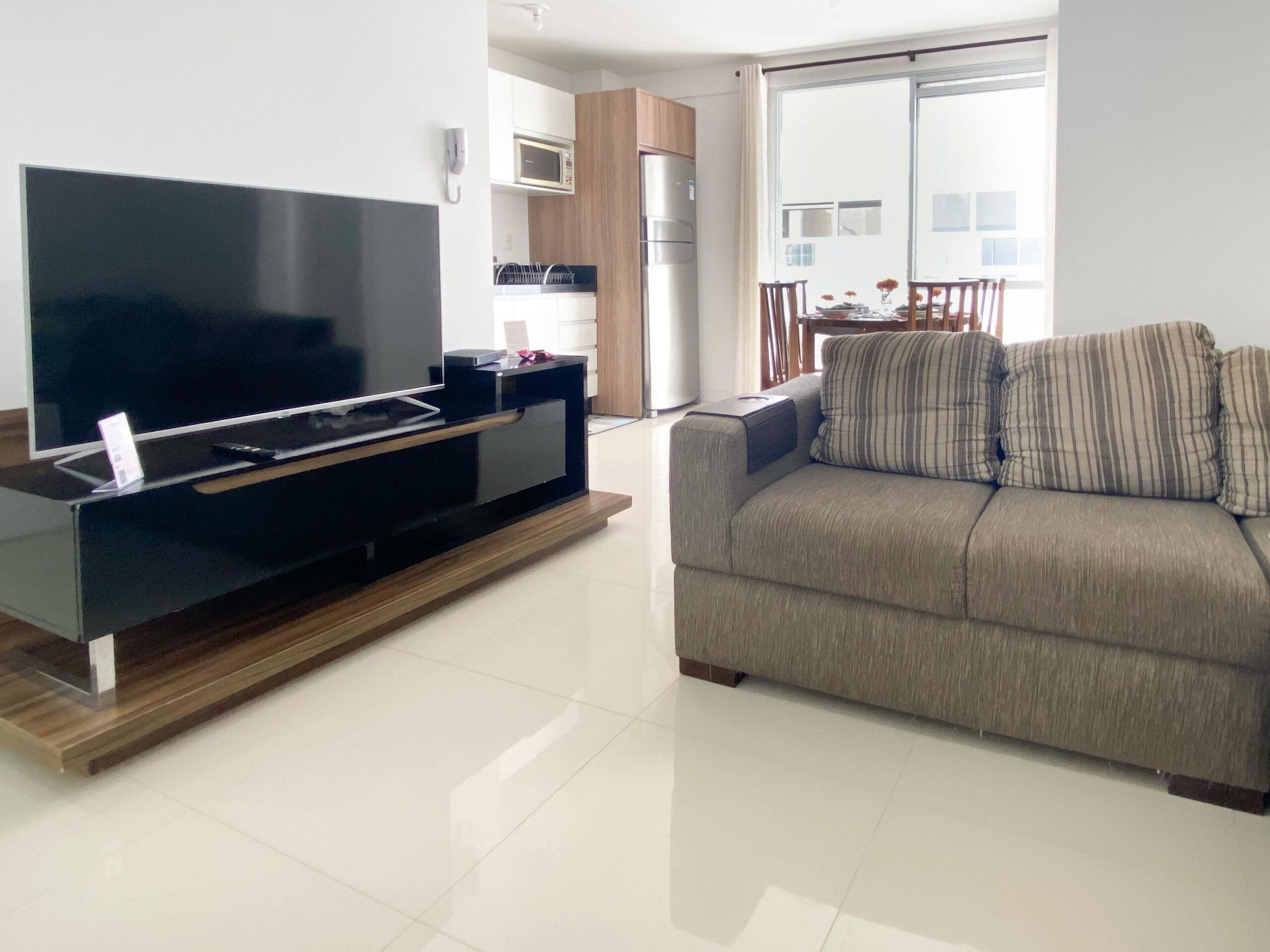 A modern living room with a flat-screen TV, a sofa, and a dining area with a table and chairs.