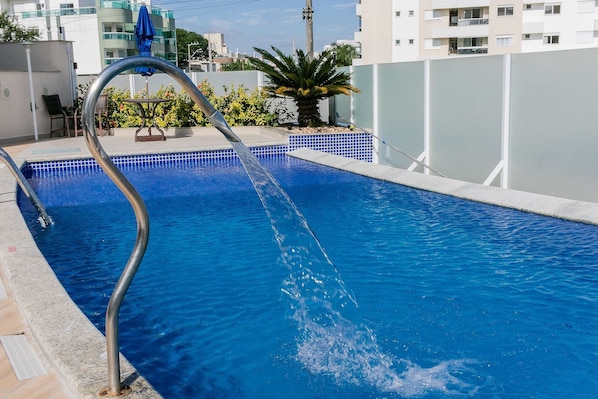 Una piscina con una escalera metálica y un borde de azulejos azules.