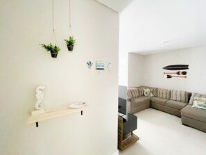 A modern living room with a sectional sofa, a wooden shelf with decorative items, and wall-mounted decorations including a seahorse, a boat, and a surfboard. - Residencial Dom Virgílio (Florianópolis)