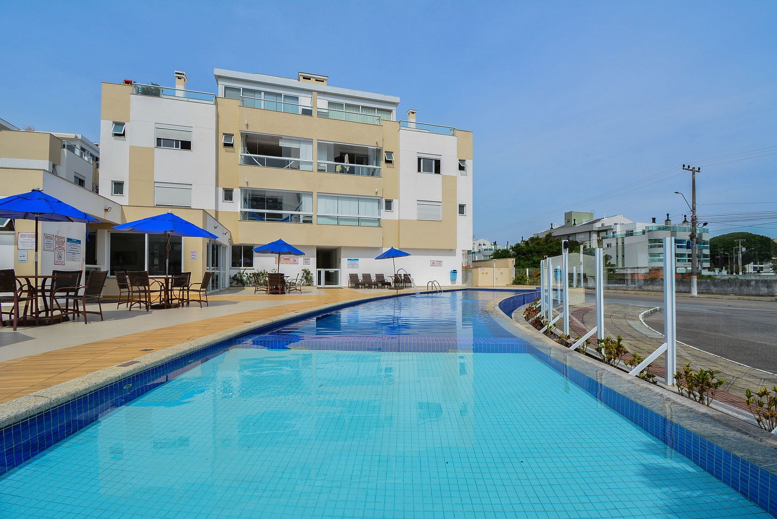 Une piscine aux carreaux bleus, entourée de chaises longues et de parasols, devant un immeuble à plusieurs étages doté de balcons.