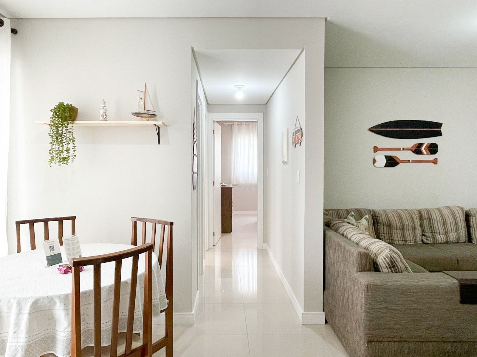 A modern living room with a sofa, a dining table with chairs, and a hallway leading to another room.