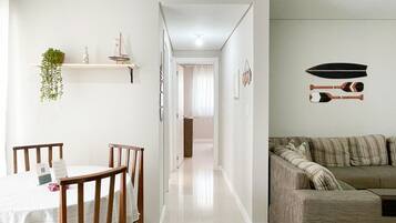 A modern living room with a sofa, a dining table with chairs, and a hallway leading to another room.