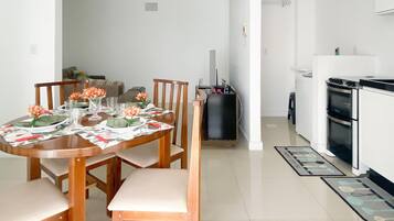 A dining area with a wooden table set for four, surrounded by chairs. A black cabinet is against the wall, and a white refrigerator is in the background.