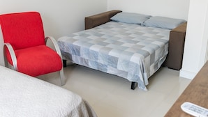 Una habitación con una cama, una silla roja y una mesa de madera.