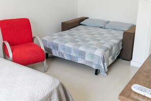 A room with a bed, a red chair, and a wooden table. - Residencial Dom Virgílio (Florianópolis)
