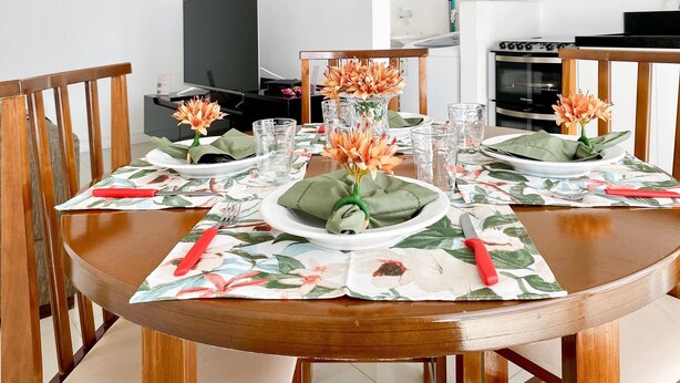 A dining table set with plates, glasses, and a flower centerpiece. - Residencial Dom Virgílio (Florianópolis)