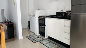 Una cocina moderna con armarios blancos, encimera negra, electrodomésticos de acero inoxidable y felpudo con estampado blanco y negro.