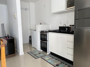 A modern kitchen with white cabinets, a black countertop, stainless steel appliances, and a black and white patterned doormat. - Residencial Dom Virgílio (Florianópolis)