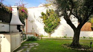 Un patio con una parrilla, un árbol con frutos naranjas y un césped bien cuidado.