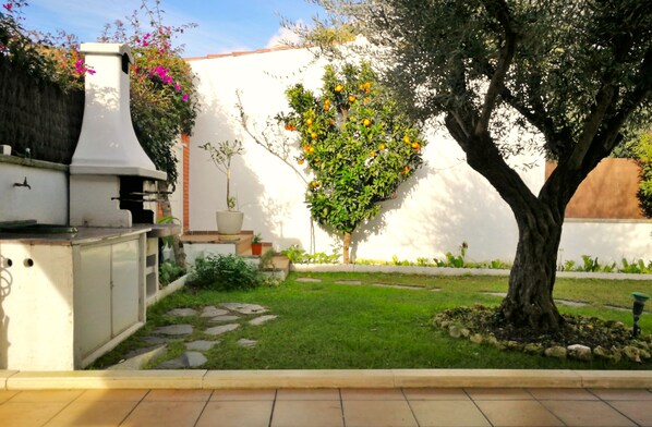 A patio area with a barbecue grill, a tree with orange fruit, and a well-maintained lawn.