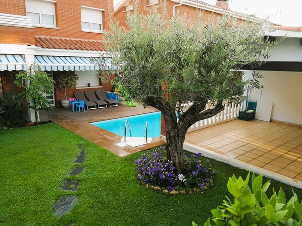 A backyard with a swimming pool, a tree, and a patio area with chairs and a table.