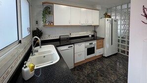 Una cocina moderna con armarios blancos, encimera negra, horno empotrado y refrigerador.