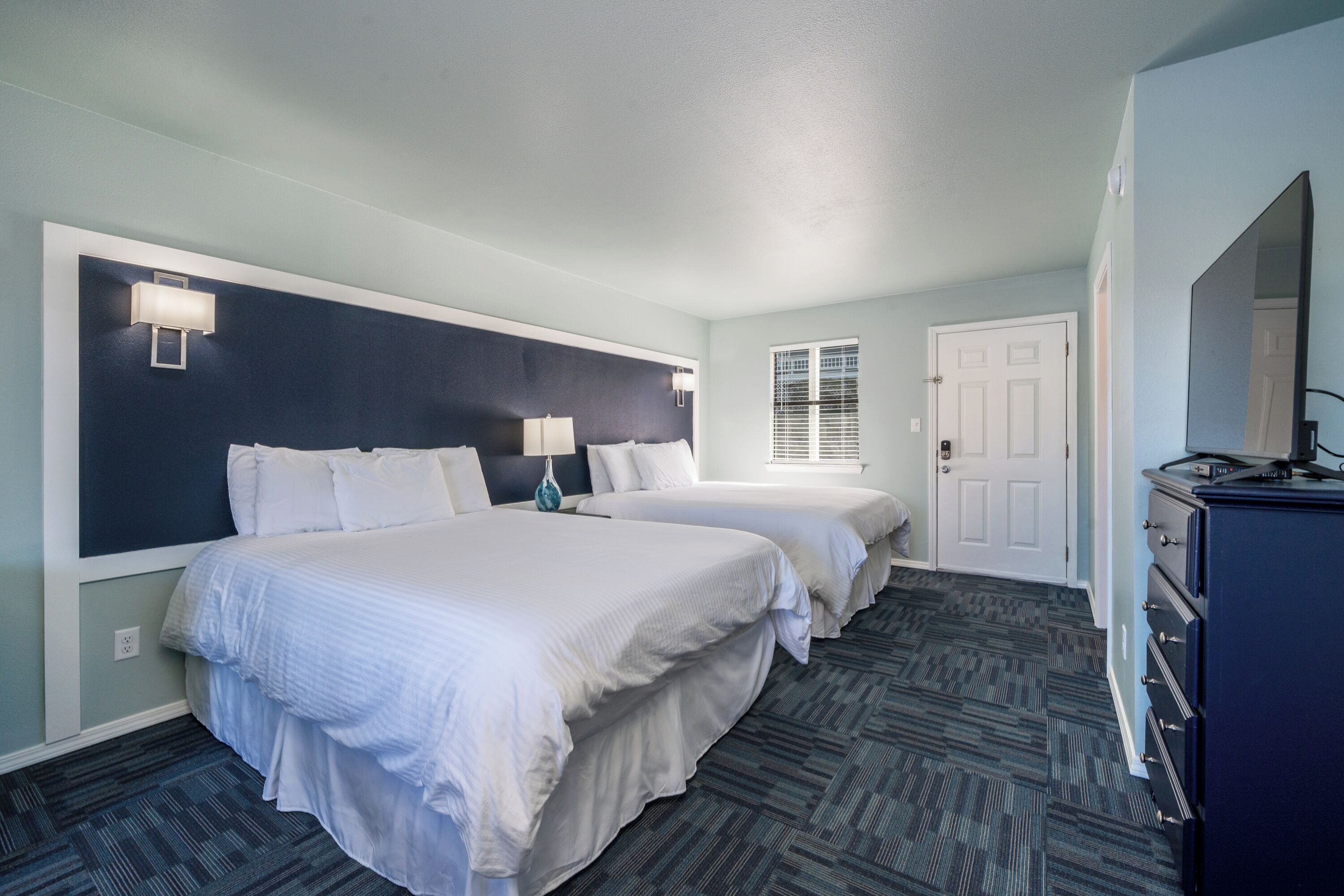 A hotel room with two beds, a dresser, and a window with blinds.