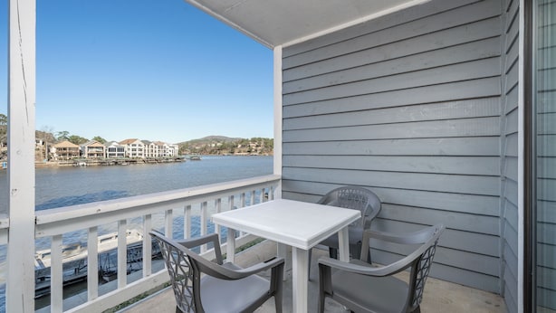 A balcony with a white table and two chairs, overlooking a body of water with boats and buildings in the background. - Deluxe Studio Suite, 2 Queen Beds, Lake View, Ground Floor (Hot Springs)