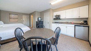 Une chambre d’hôtel comprenant un lit, une table à manger avec des chaises, une kitchenette équipée de placards et d’appareils électroménagers, et un téléviseur.