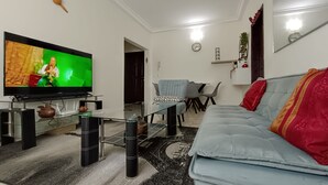 A living room with a flat-screen TV, a sofa, a dining table, and a kitchen area. - Quiet and Secure Apartment in Angré 9e Tranche, Abidjan, A Haven of Peace. (Abidjan Cocody Angre 9ieme Tr.)