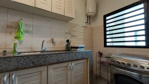A kitchen with cabinets, a sink, a window with blinds, and an oven. - Quiet and Secure Apartment in Angré 9e Tranche, Abidjan, A Haven of Peace. (Abidjan Cocody Angre 9ieme Tr.)