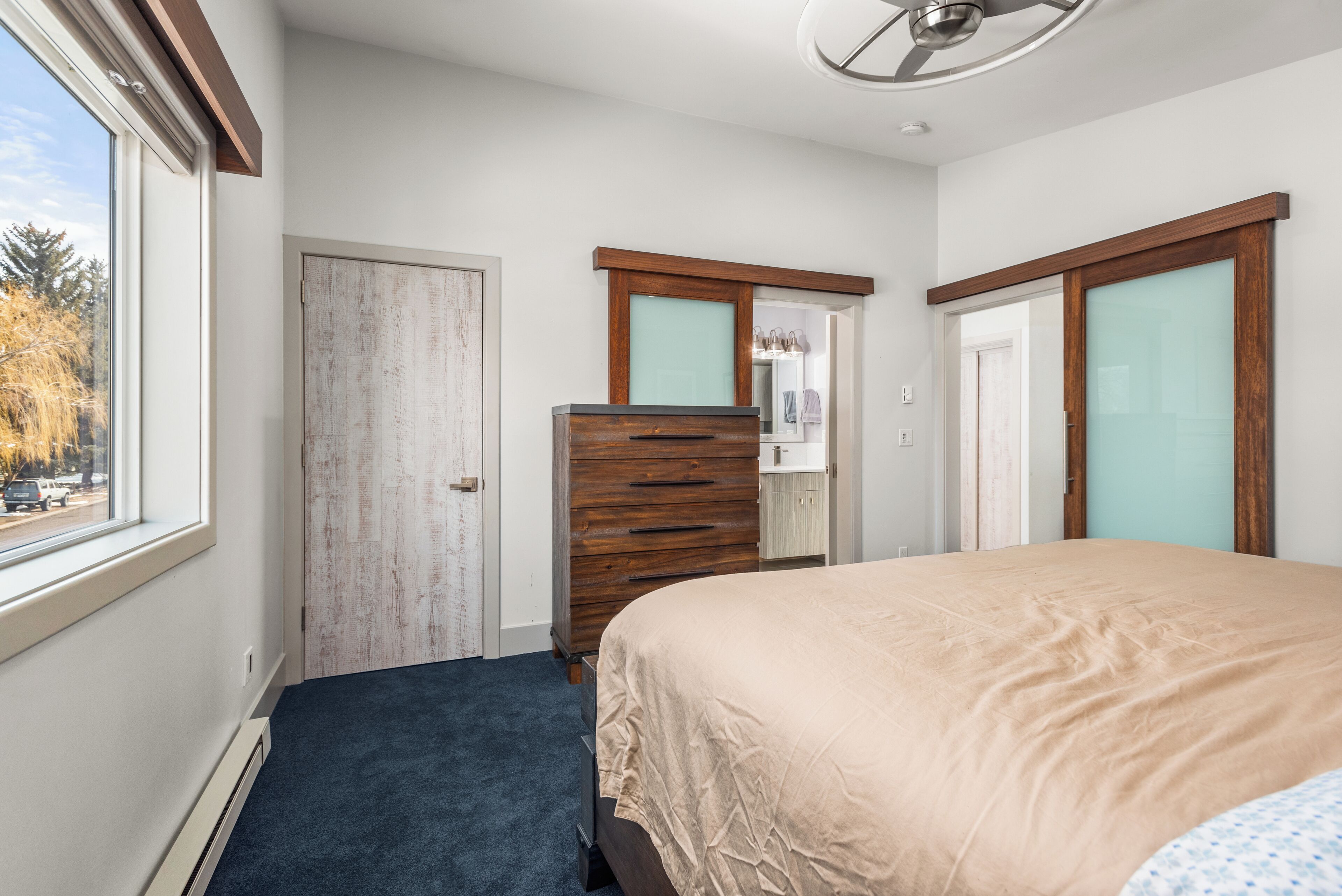 Un dormitorio con cama, cómoda y ventana que ofrece vistas a árboles y una carretera.
