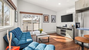Un salón moderno con un sofá azul, una mesa de centro y una zona de cocina con un refrigerador y un televisor de pantalla plana.