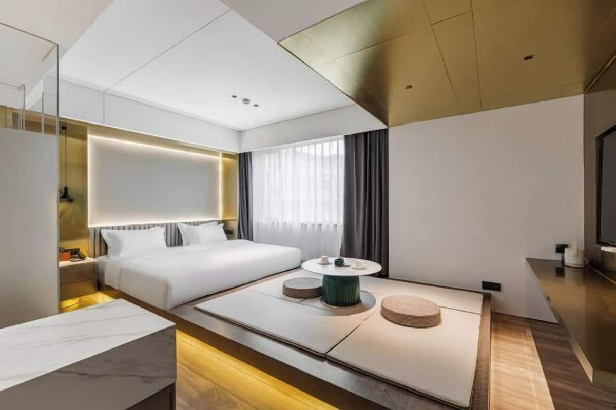 Une chambre d’hôtel moderne, équipée d’un lit, d’une table basse ronde, d’un téléviseur et d’une grande fenêtre avec des rideaux.