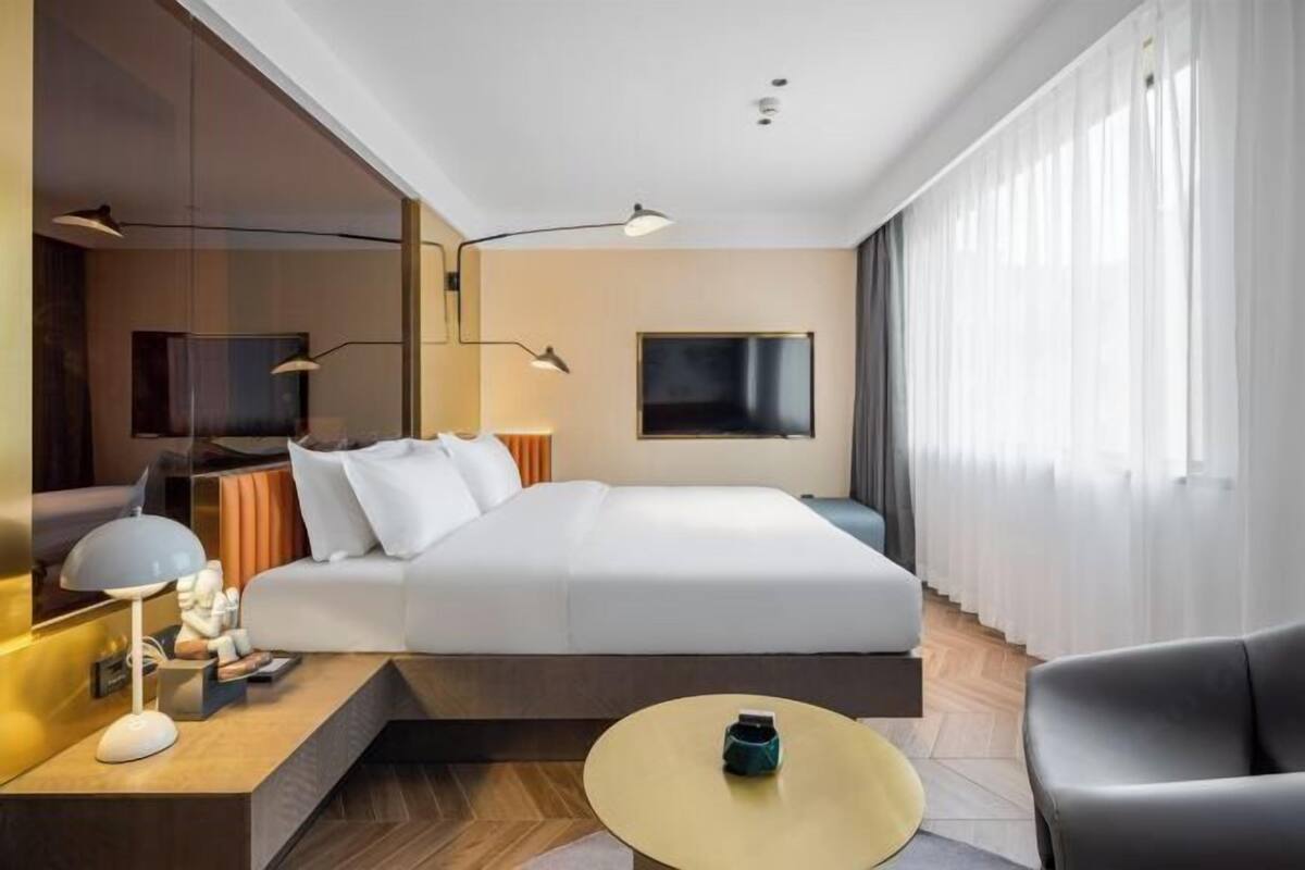 Une chambre d’hôtel moderne équipée d’un lit, d’une table de chevet, d’une lampe, d’une télévision et offrant une vue sur l’extérieur.