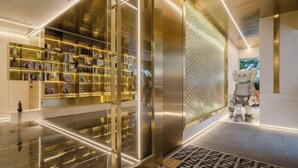 A modern lobby with a large, illuminated bookshelf, a patterned wall, and a robot sculpture.
