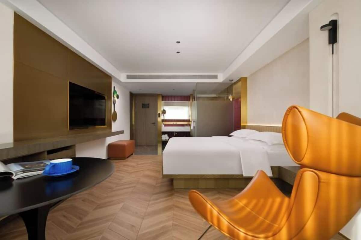 Une chambre d’hôtel avec un lit, une télévision, une table sur laquelle se trouve un bol bleu, et une chaise.