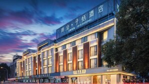 A modern hotel with a prominent sign, multiple floors, and a row of shops at the ground level.