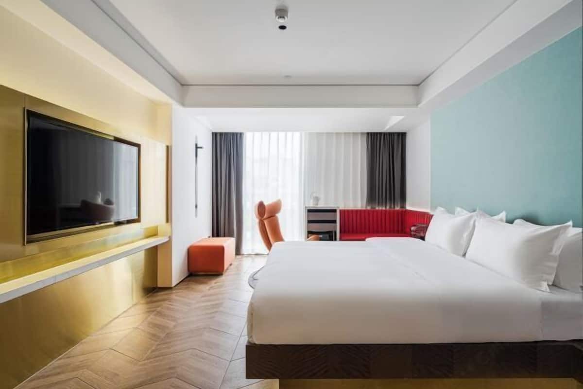 Une chambre d’hôtel dotée d’un grand lit, d’un téléviseur à écran plat fixé au mur, d’un bureau avec une chaise et d’une fenêtre avec des rideaux.