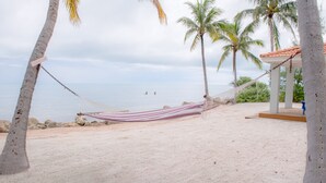 Una hamaca atada entre palmeras en una playa arenosa con vista al océano.