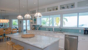 Una cocina moderna con una isla grande, armarios blancos y vistas al océano.